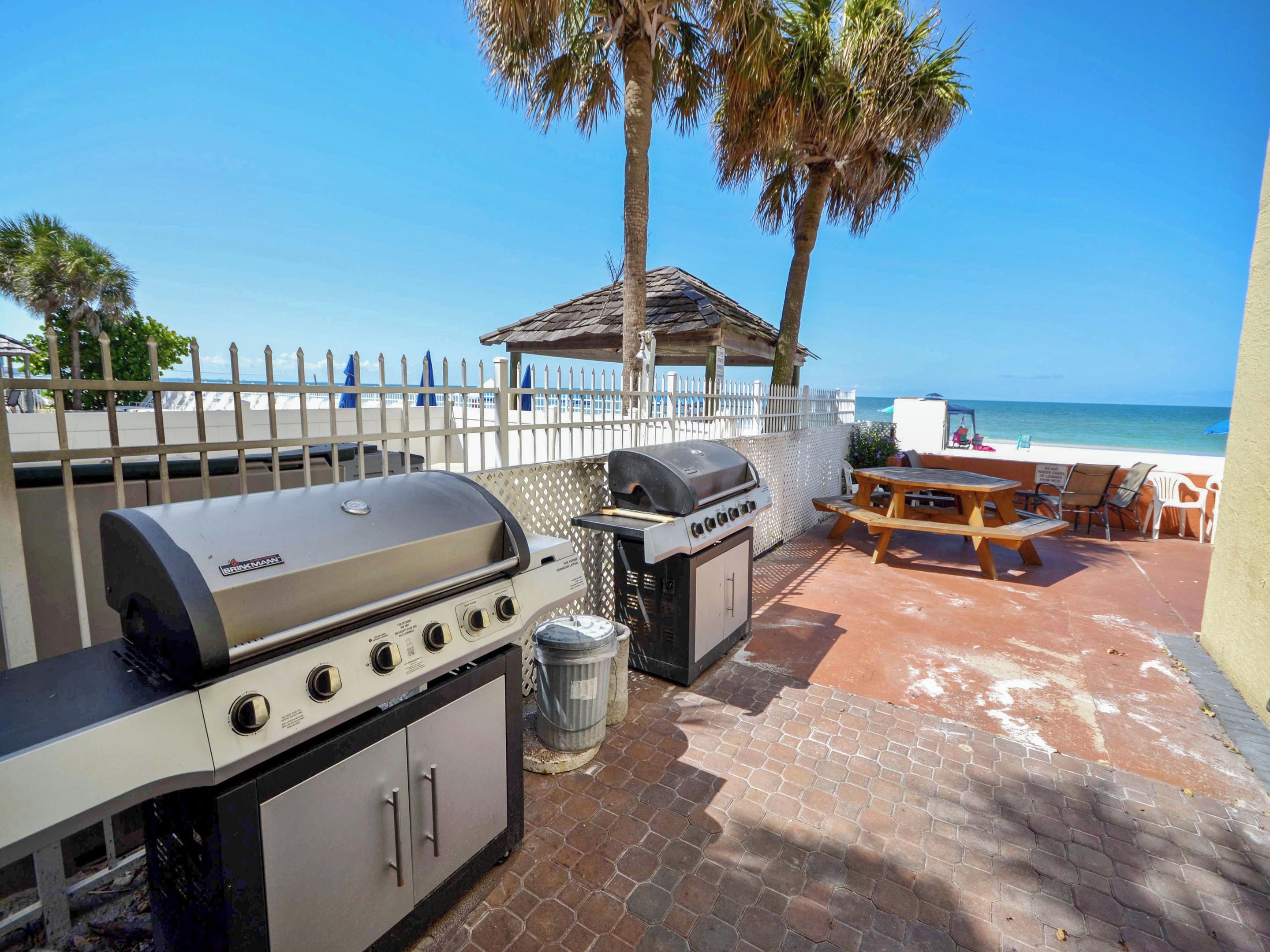 Un patio exterior con una parrilla, una mesa y sillas, con vista a una playa.