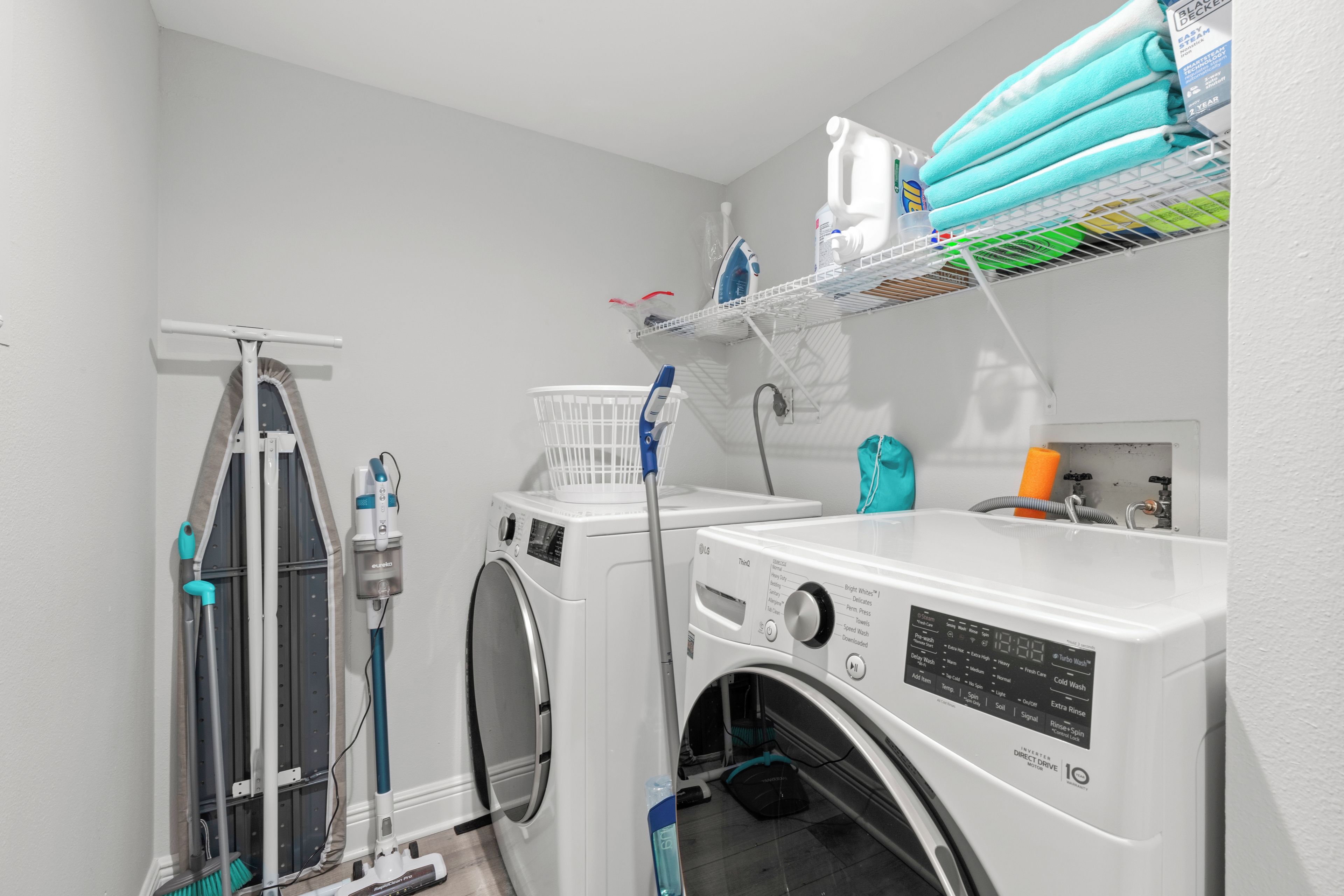 A laundry room with two front-loading washing machines, a floor scrubber, and a shelf with laundry supplies.