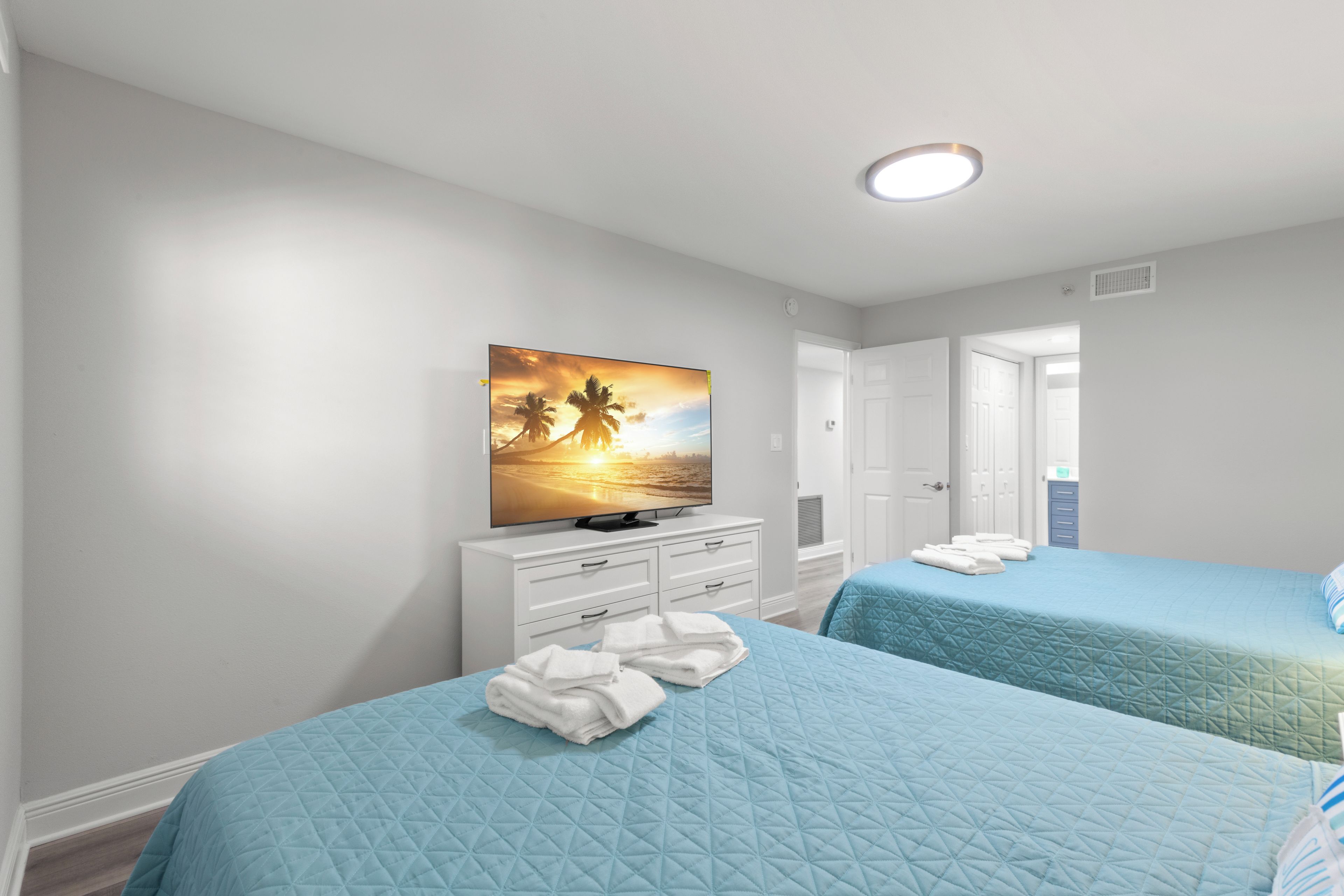 A hotel room with two beds, a TV on a dresser, and a painting on the wall.