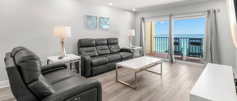Un salón moderno con un sofá de cuero negro, una mesa de centro blanca y un balcón con vistas al mar.