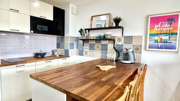 A modern kitchen with a wooden island, white cabinets, a black microwave, and a colorful backsplash.