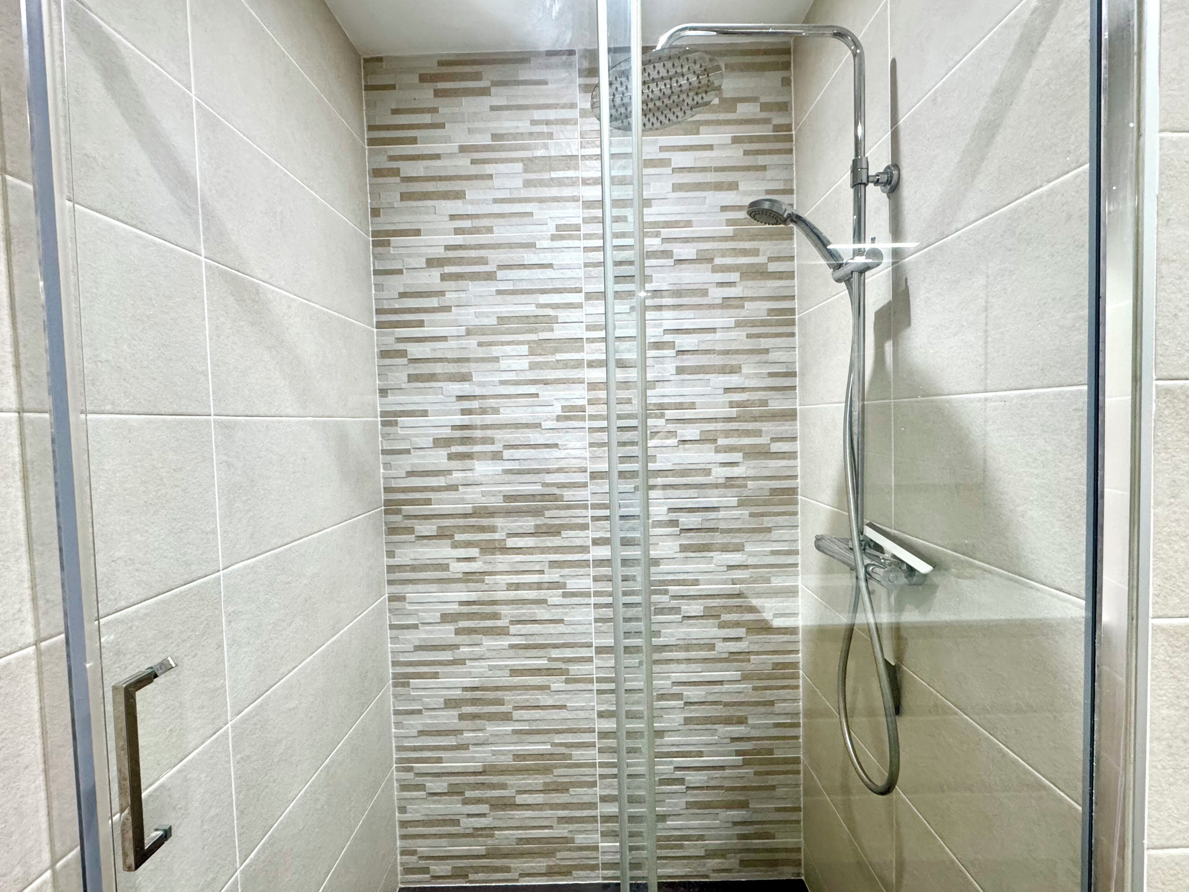A shower area with a glass door, a showerhead, and a handheld shower attachment.