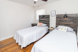 A bedroom with two single beds, a wooden headboard, a bedside table with a lamp, and a framed picture on the wall.