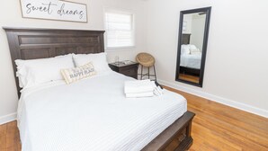 A bedroom with a bed, a nightstand, a chair, a mirror, and a ceiling fan. - 2 bed/1 ba-across f/Coliseum/GAC (Greensboro)