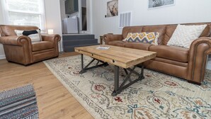 A living room with a brown leather sofa, two brown leather armchairs, a wooden coffee table, and patterned rugs. - 2 bed/1 ba-across f/Coliseum/GAC (Greensboro)