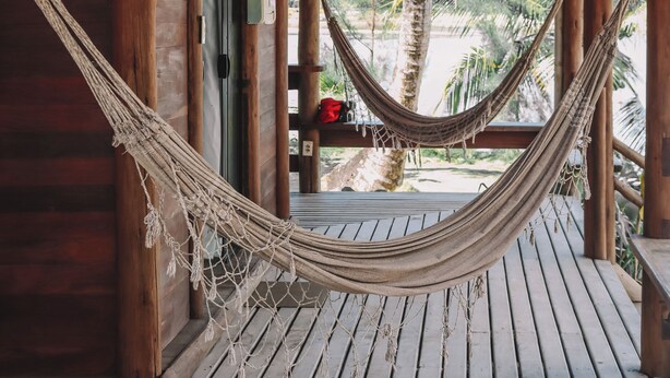 A wooden structure with a hammock hanging in the center, a door, and a view of palm trees and a beach. - Pôr do Sol Eco Suítes (Maraú)