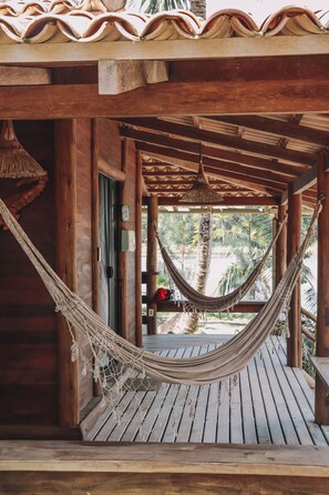 A wooden structure with a hammock hanging in the center, a door, and a view of palm trees and a beach. - Pôr do Sol Eco Suítes (Maraú)