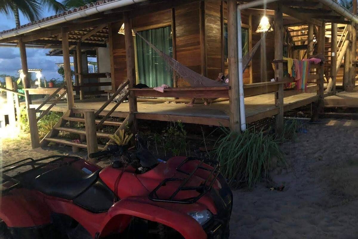 Une maison de plage en bois, dotée d’un porche, d’un hamac et d’un quad rouge en premier plan.