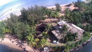 An aerial view of a beachside property with a house surrounded by palm trees and a sandy beach. - Pôr do Sol Eco Suítes (Maraú)