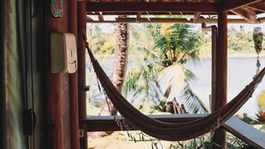 A wooden deck with a hammock, wooden ceiling, and a view of palm trees and water. - Pôr do Sol Eco Suítes (Maraú)