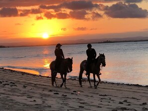 Deux personnes à cheval, se promenant le long d’une plage au coucher du soleil.