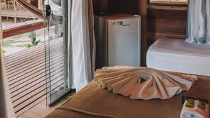 A room with a bed, a small refrigerator, a window with curtains, and a hammock outside. - Pôr do Sol Eco Suítes (Maraú)