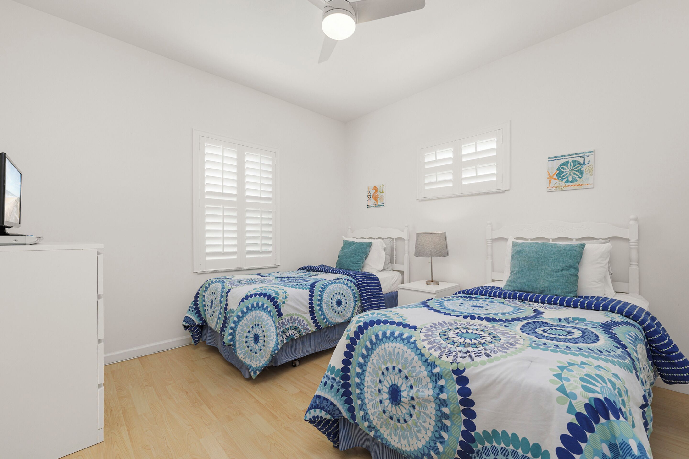 A bedroom with two beds, white walls, and a ceiling fan.