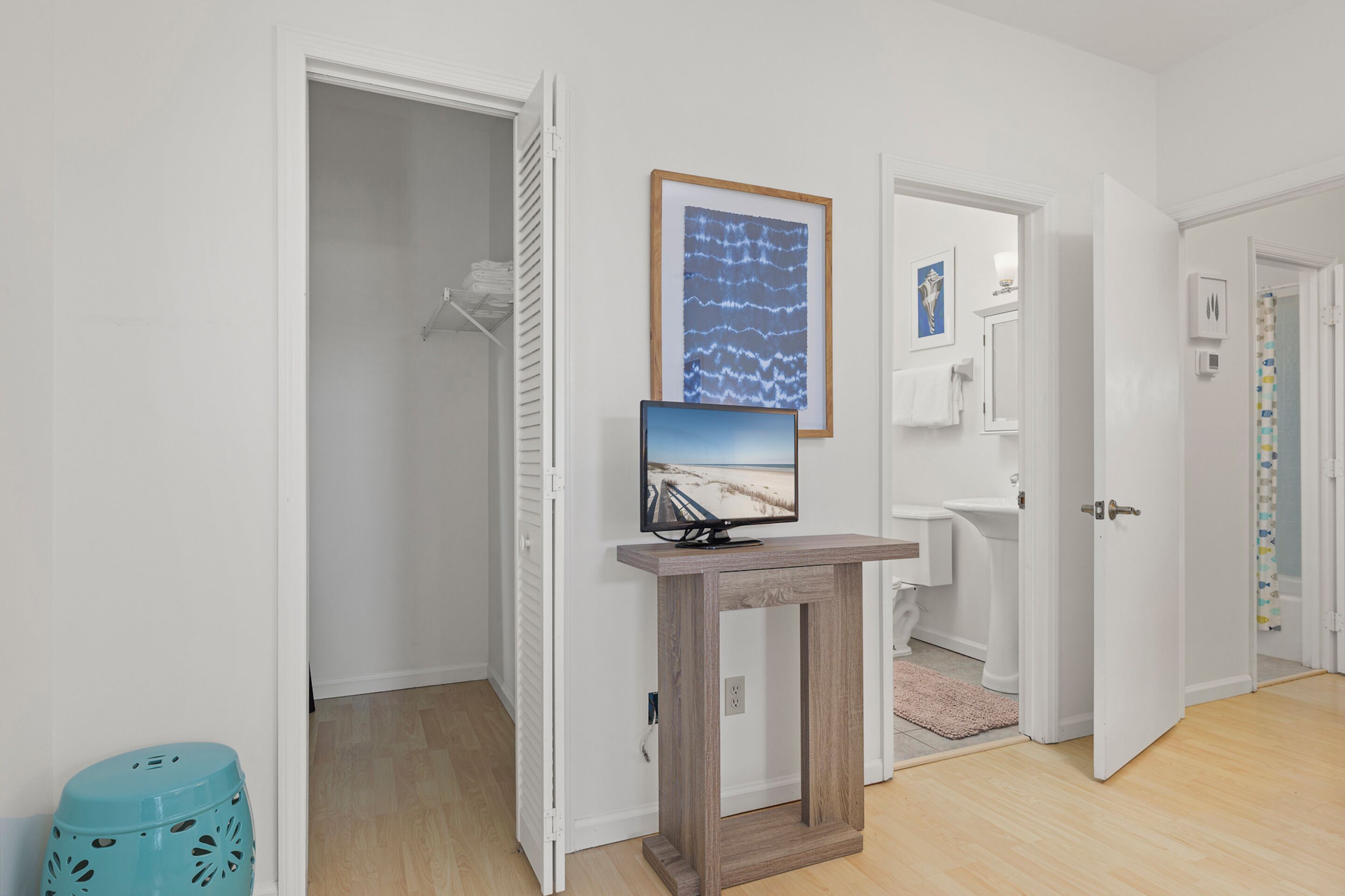 A hallway with a wooden console table displaying a TV, a door leading to a bathroom, and a closet with hanging clothes.