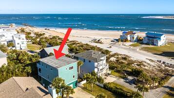 A coastal residential area with a prominent turquoise building, a beach, and a clear view of the ocean.