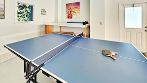 Una mesa de ping pong con red, una raqueta y un estante empotrado en la pared con una cámara.