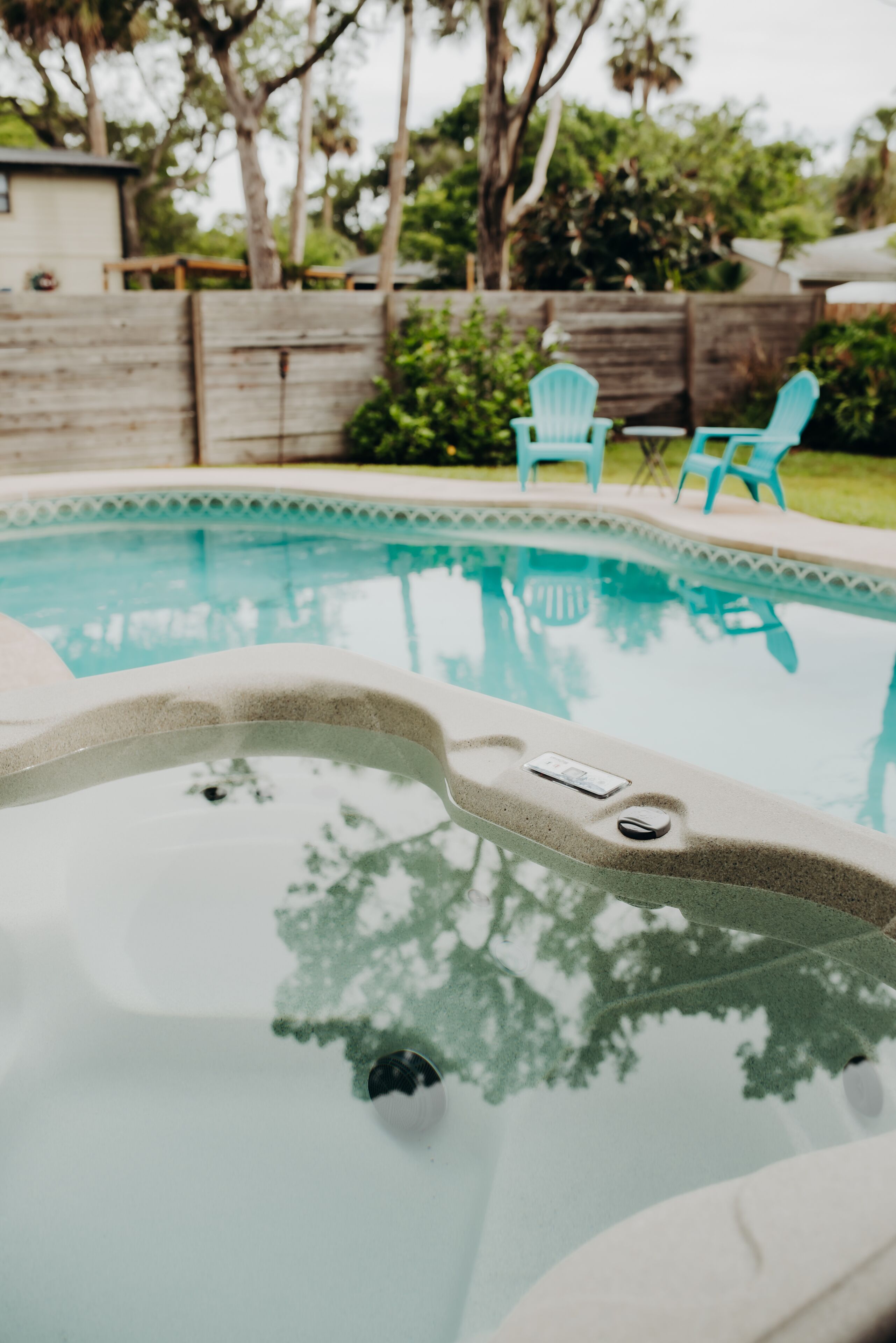 Una piscina con un jacuzzi, rodeada por una valla de madera, y dos sillas azul claro al fondo.