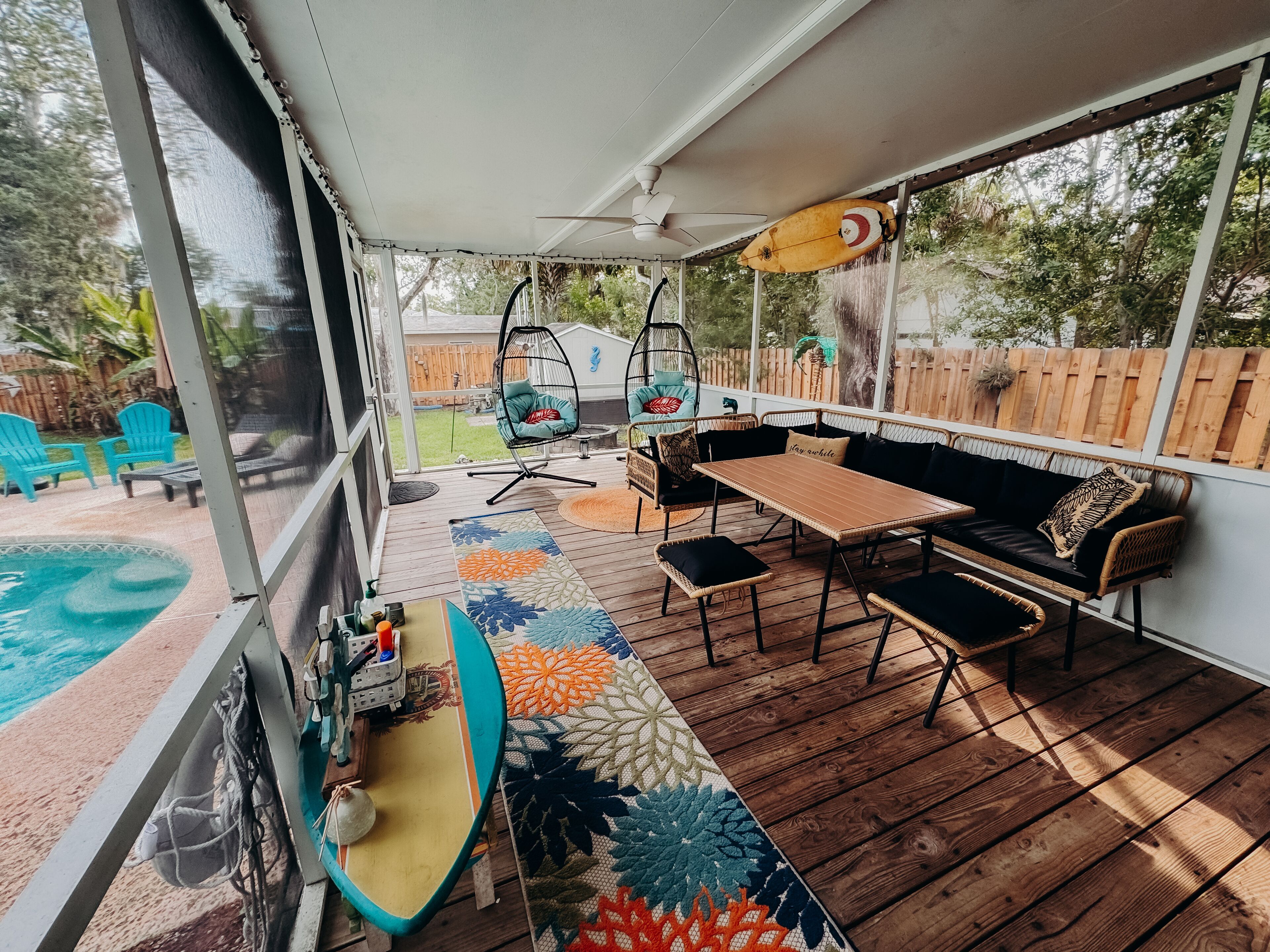En udendørs terrasse med pool, træterrasse, hængestol, sofa og bord.