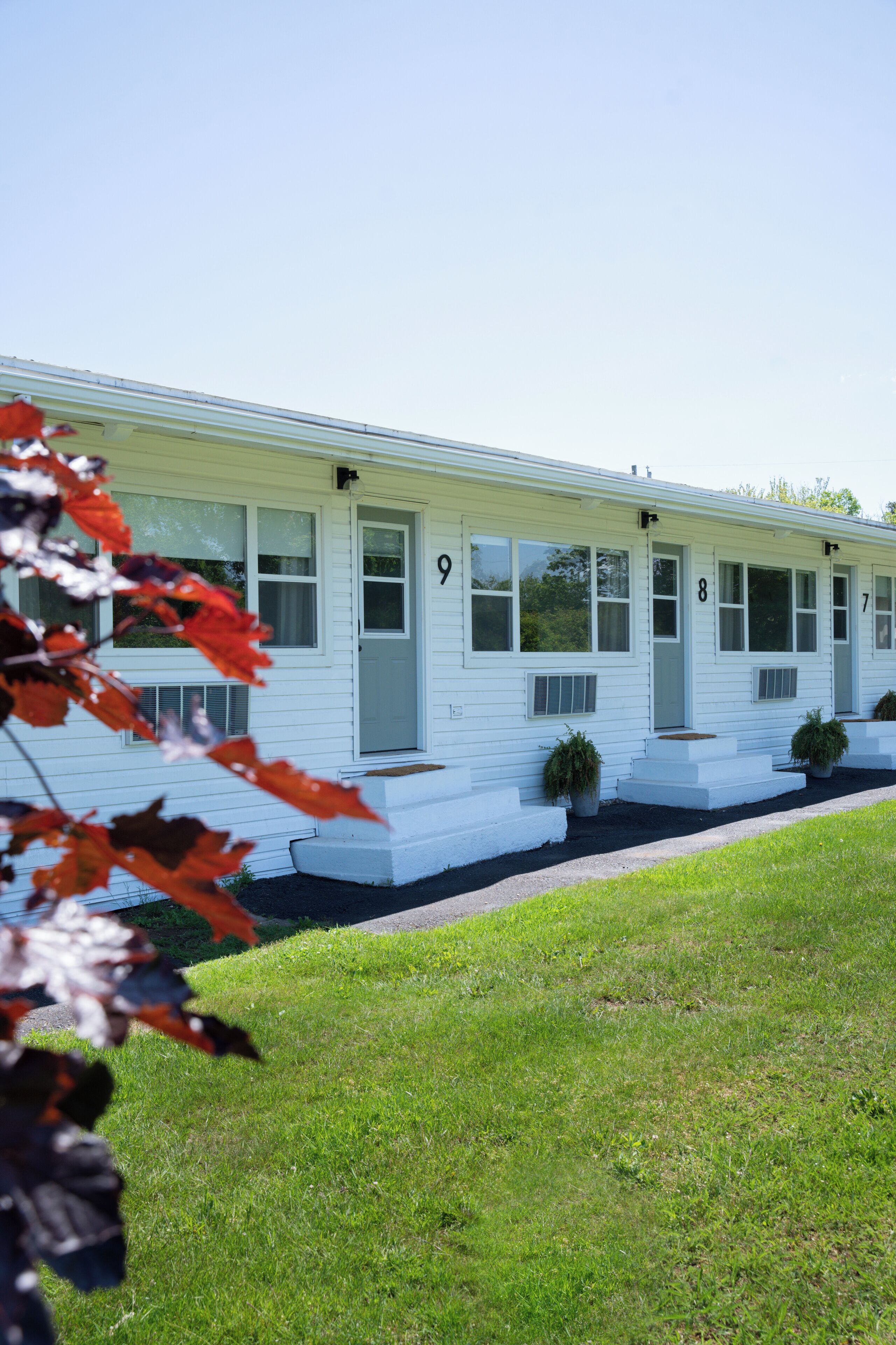 A white motel with numbered doors, a covered porch, and potted plants.