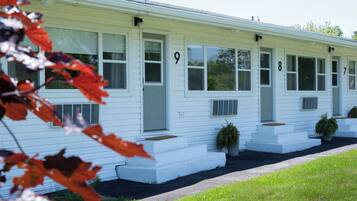 A white motel with numbered doors, a covered porch, and potted plants.
