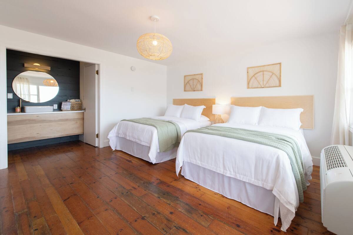 A hotel room with two beds, a wooden floor, a large mirror, and a ceiling light fixture.
