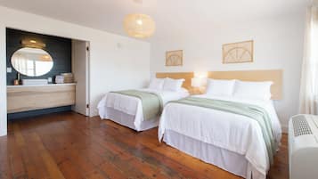 Een hotelkamer met twee bedden, een houten vloer, een grote spiegel en een plafondlamp.