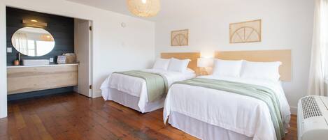 A hotel room with two beds, a wooden floor, a large mirror, and a ceiling light fixture.