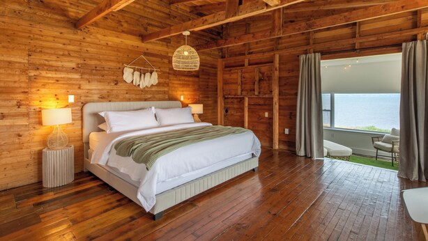 Quarto de cabana de madeira com cama, luminárias de cabeceira e vista para o exterior.