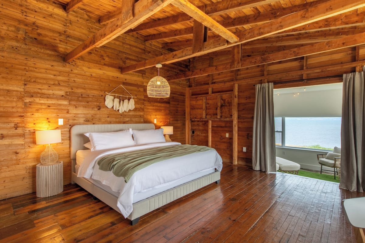 A wooden cabin bedroom with a bed, bedside lamps, and a view of the outdoors.
