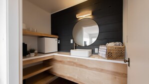 Uma casa de banho moderna com toucador de madeira, uma pia branca e um espelho redondo.