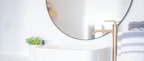A bathroom with a white sink, gold faucet, and a round mirror.
