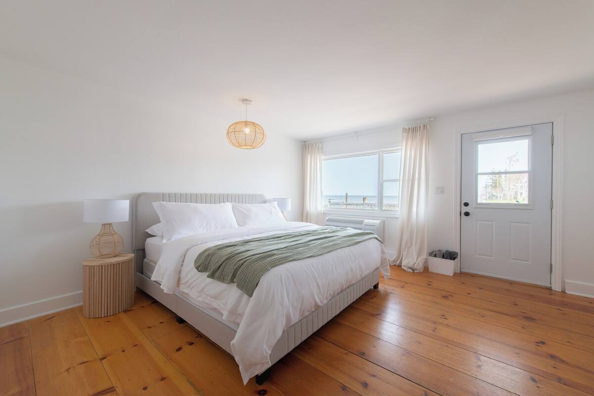 A bedroom with a bed, a bedside lamp, a window with curtains, and a door.