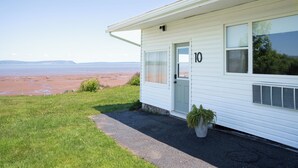 Uma casa térrea branca com o número 10 na porta, um pequeno alpendre e vista para a praia.