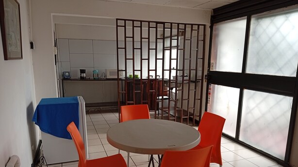 Un comedor con una mesa redonda y cuatro sillas naranjas, un mantel azul y una cocina al fondo.