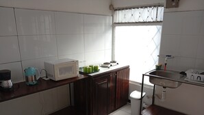 Una cocina con azulejos blancos, un ventanal con persianas, un lavabo y un microondas.