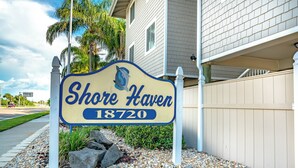 A sign for Shore Haven at 18720, surrounded by pebbles and a white fence. - Shore Haven Unit 5A by Distinctive Beach Rentals (Indian Shores)