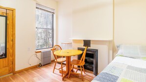 Een kamer met houten vloer, een ronde tafel met twee stoelen, een open haard en een bed met sprei.