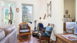 A cozy room with a wooden rocking chair, a cushioned chair, and a sofa. There is a window with a view of greenery outside. - Siete Caballos by Kokopelli Property Management (Santa Fe)