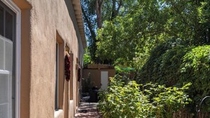 A narrow pathway leading to a building with a beige exterior, surrounded by lush greenery and trees. - Siete Caballos by Kokopelli Property Management (Santa Fe)