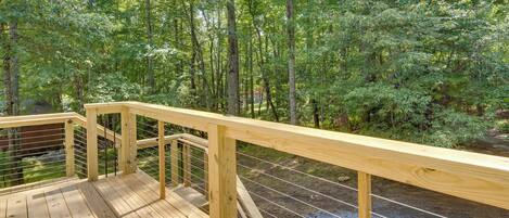 A wooden deck with a metal railing overlooking a forested area.