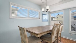 A dining area with a wooden table and chairs, light blue walls, and a chandelier. - Sunset Beach House by Distinctive Beach Rentals (Treasure Island)