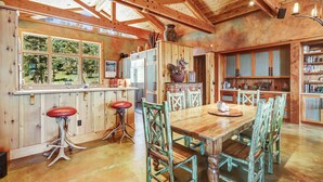 A rustic kitchen with wooden beams, a large wooden table, and bar stools.
