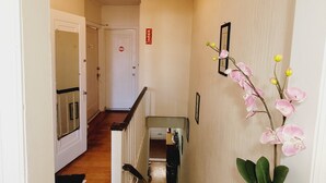 A hallway with a wooden floor, white walls, a staircase, and a vase with orchids. - Enjoy this Cozy Brooklyn Room with Parking & Shared Kitchen & Bathroom (Brooklyn)