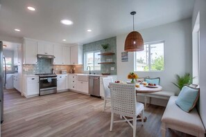 A modern kitchen with white cabinetry, a dining area with a round table, and a built-in bench.