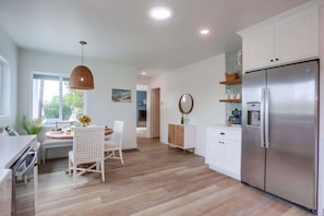 Une cuisine moderne avec un coin repas, des meubles blancs, un réfrigérateur en acier inoxydable et un luminaire suspendu.