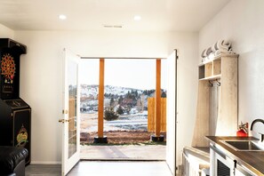 A room with a door leading to a snowy outdoor area, a dartboard, and a wooden shelf with towels.