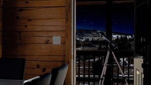 L’intérieur d’un chalet en bois, avec un télescope sur un balcon donnant sur un paysage enneigé, sous un ciel étoilé.