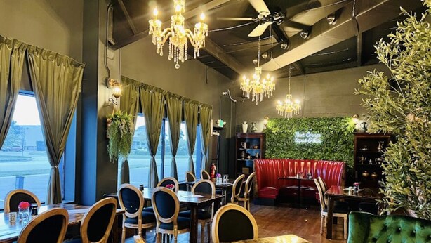 Un restaurante con mesas y sillas de madera, un banco tapizado en verde y candelabros colgantes.