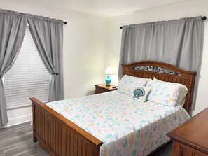 Ein Schlafzimmer mit einem hölzernen Bett, grauen Vorhängen, einer Nachttischlampe und einer gemusterten Tagesdecke.