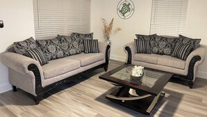 Una sala de estar con dos sofás grises, cojines estampados en blanco y negro, una mesa de centro de vidrio y una decoración de pared con una tortuga.